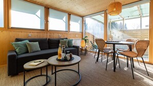 A cozy room with a sofa, two round tables, wicker chairs, and large windows. - Cocci-vert à L'oasis des Coccinelles (Sainte-Croix-aux-Mines)
