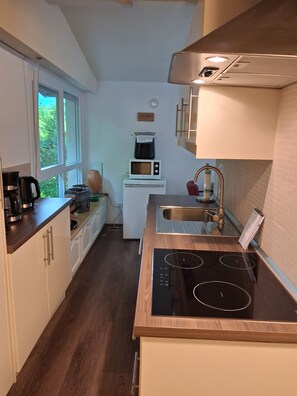 A compact kitchen with a built-in microwave, stove, and sink. There is a window providing natural light and a view of greenery outside.