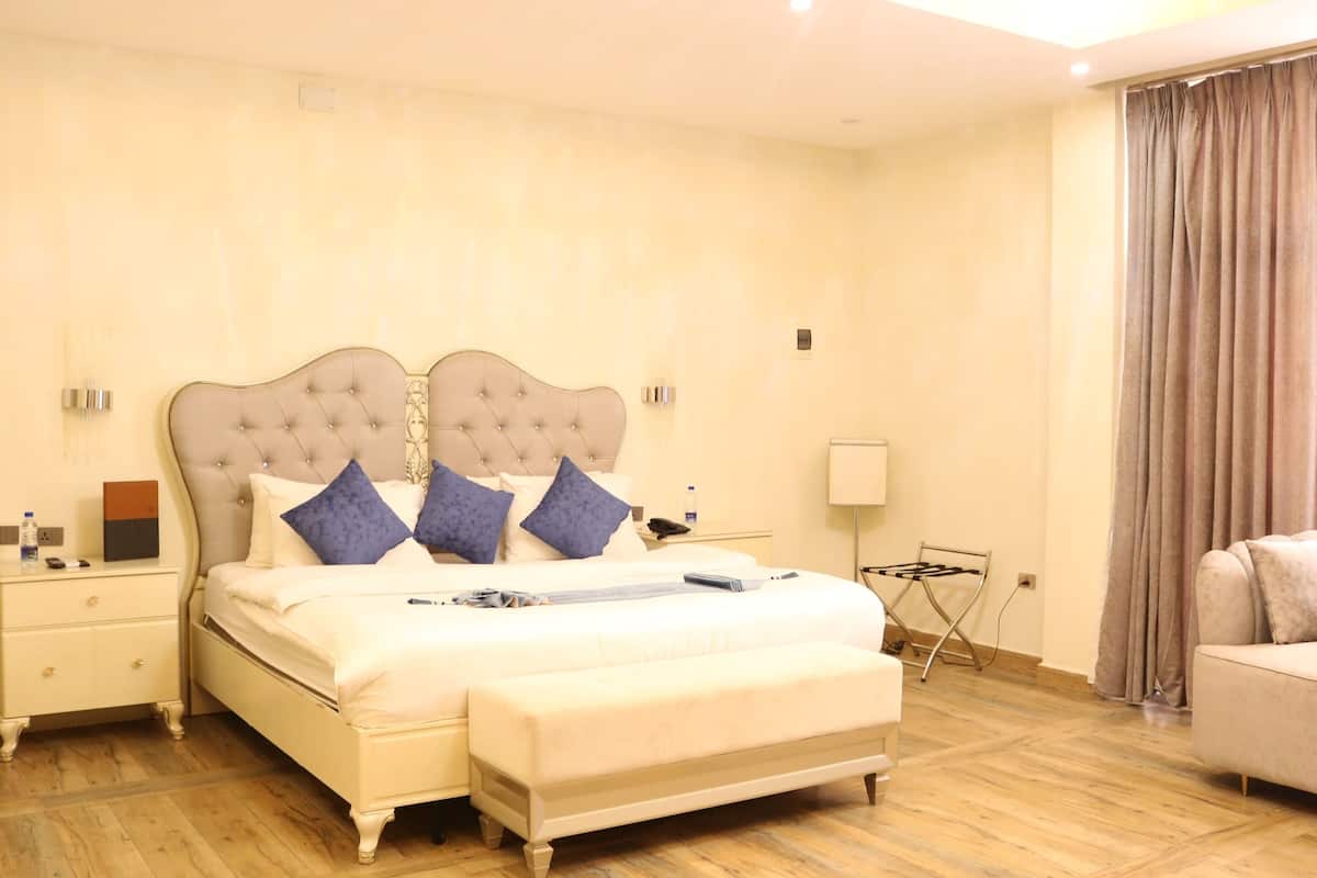 A spacious bedroom with a large bed, a bedside table, a nightstand, a sofa, and a window with curtains.