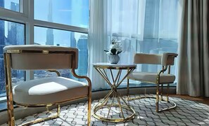 Una habitación moderna con un ventanal que ofrece vistas de la ciudad, una mesa redonda con un florero y dos sillas con marco dorado.