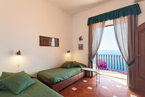 Ein Zimmer mit zwei Betten, einem Balkon mit Meerblick und einer Tür.