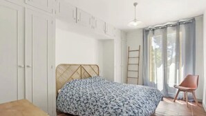 A bedroom with a bed, a wardrobe, a chair, and a window with curtains.