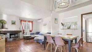 A spacious living area with a fireplace, a dining table with chairs, a sofa, and a large window with curtains.
