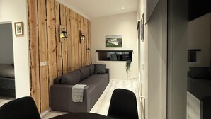 A modern living room with a grey sofa, a dining table, and a wooden accent wall.