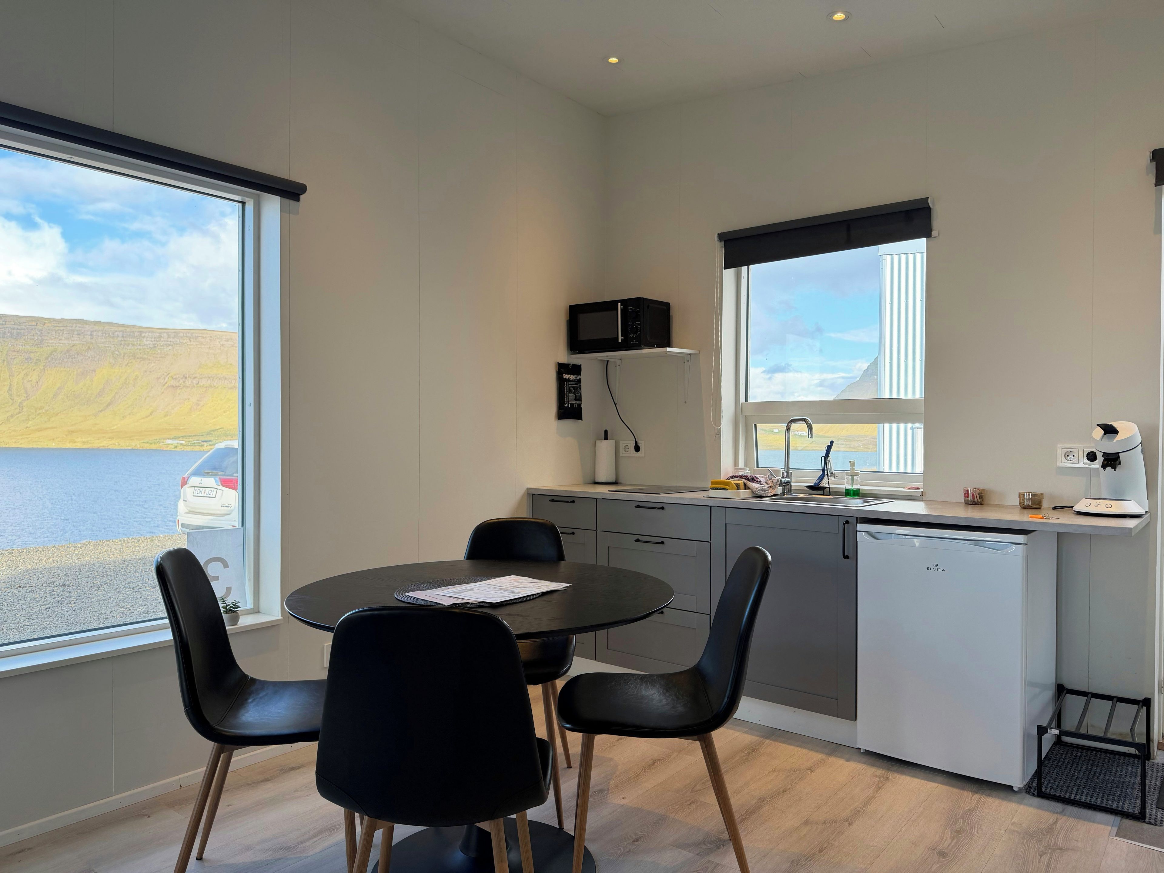 Cozinha moderna com vista para um lago, área de jantar com cadeiras pretas e uma máquina de lavar louça branca.
