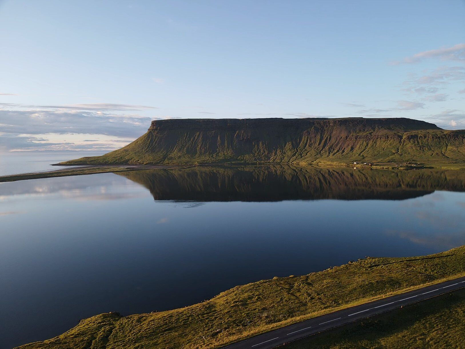 Une grande colline au sommet plat, surmontée d’un lac paisible qui reflète sa forme, entourée de verdure et bordée d’une route.