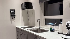 A modern kitchen with a double sink, a microwave, a window with a view, and a 'Cooking' sign on the wall.