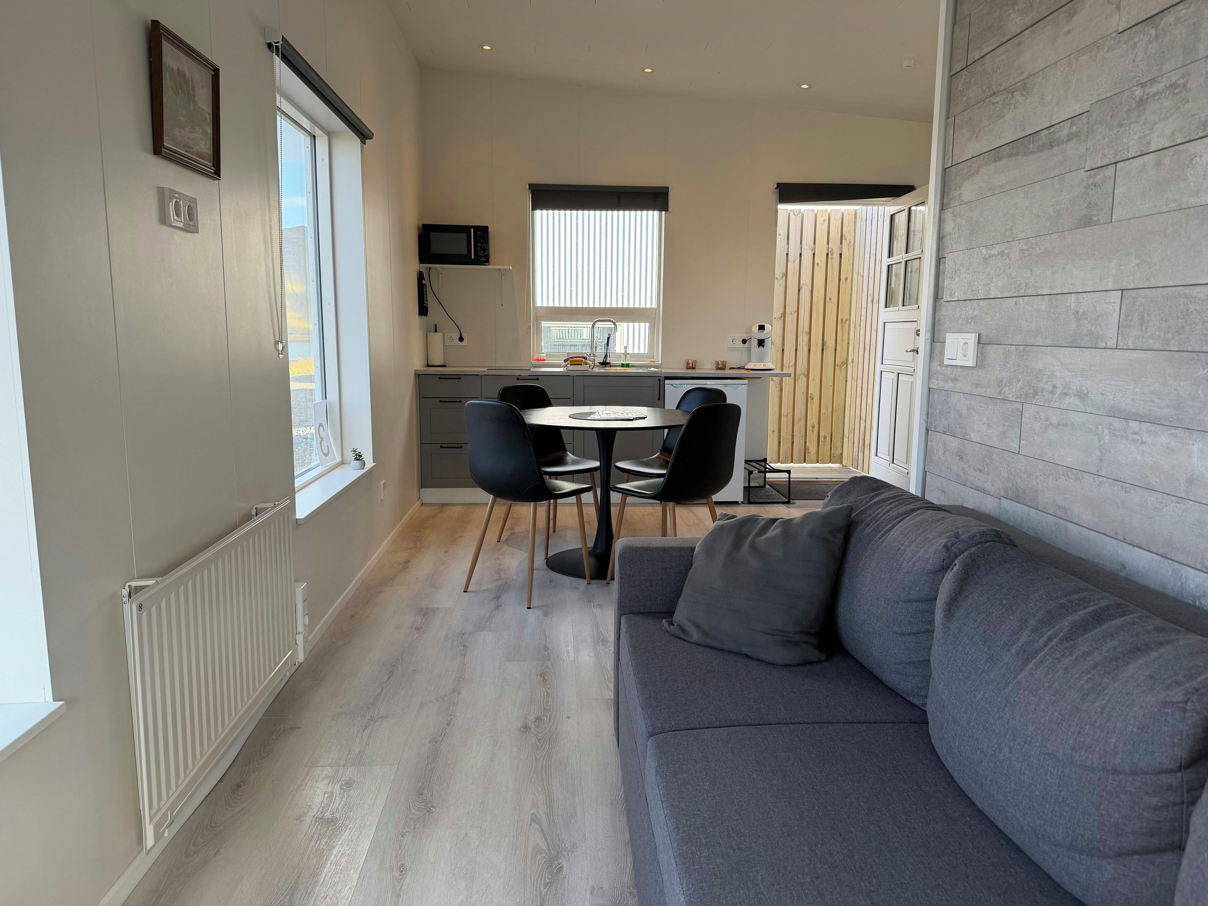 A compact living space with a dining area, kitchenette, and a grey sofa.