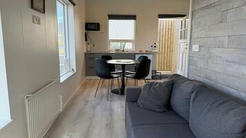Un espacio habitable compacto con comedor, kitchenette y un sofá gris.