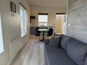 Un espace de vie compact comprenant un coin repas, une kitchenette et un canapé gris.