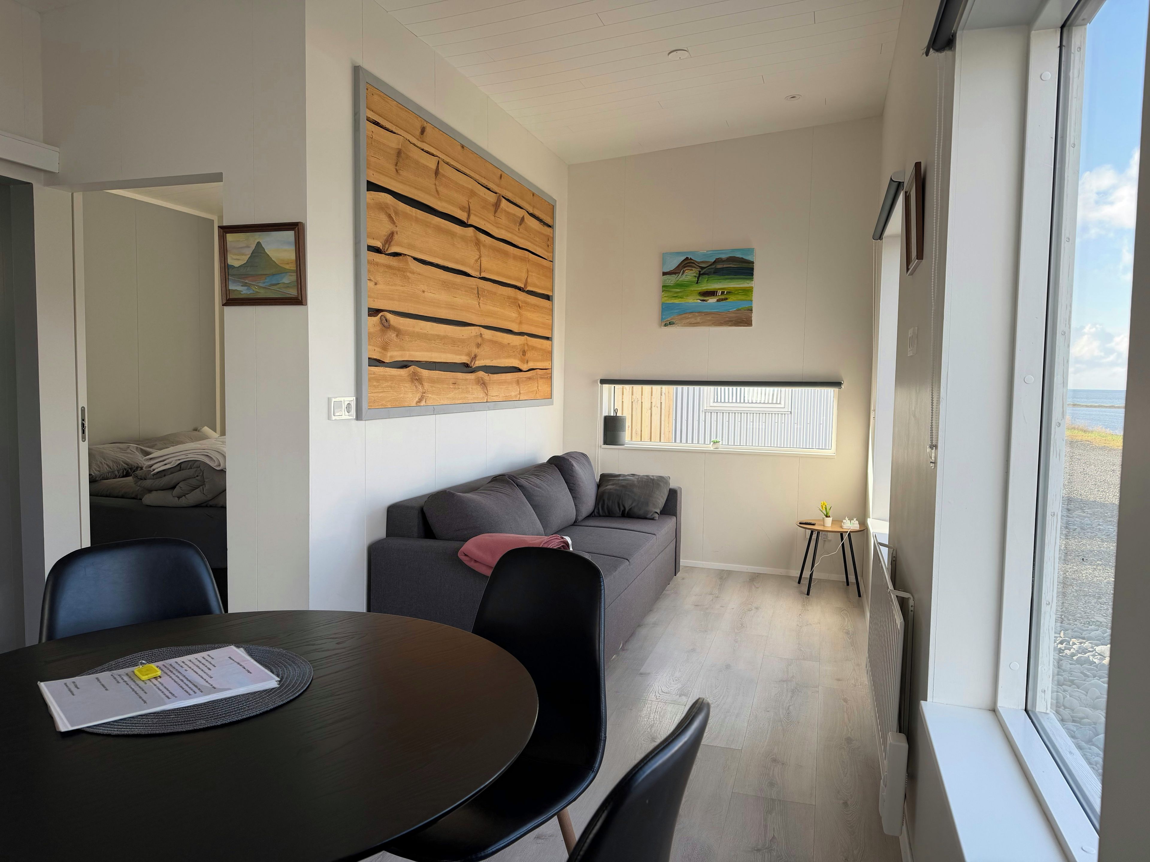 A modern living room with a sofa, a dining table with a placemat, a painting, and a window with a view.