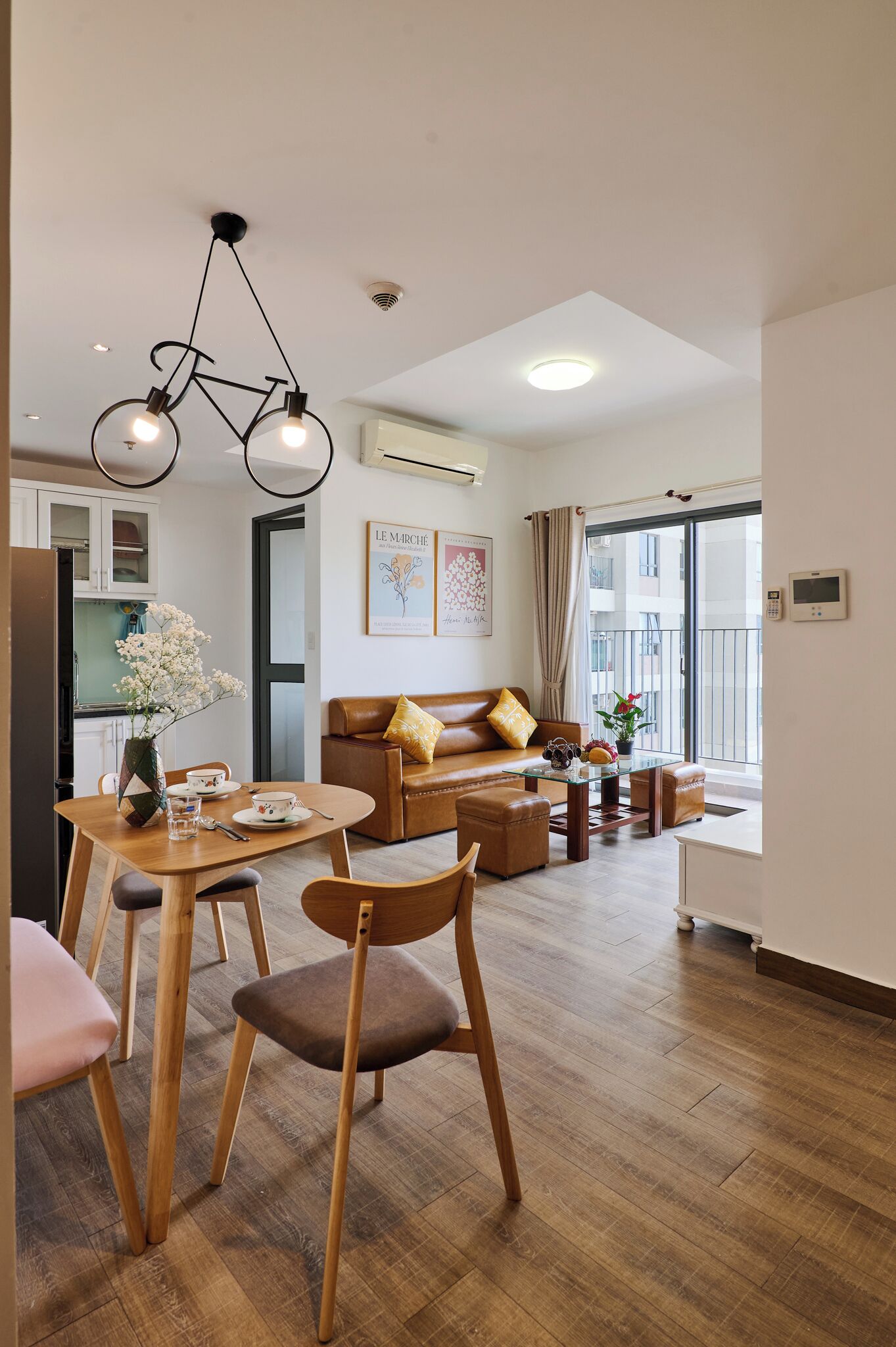 A modern living room with a dining area, wooden flooring, a sofa, a coffee table, and a hanging light fixture.