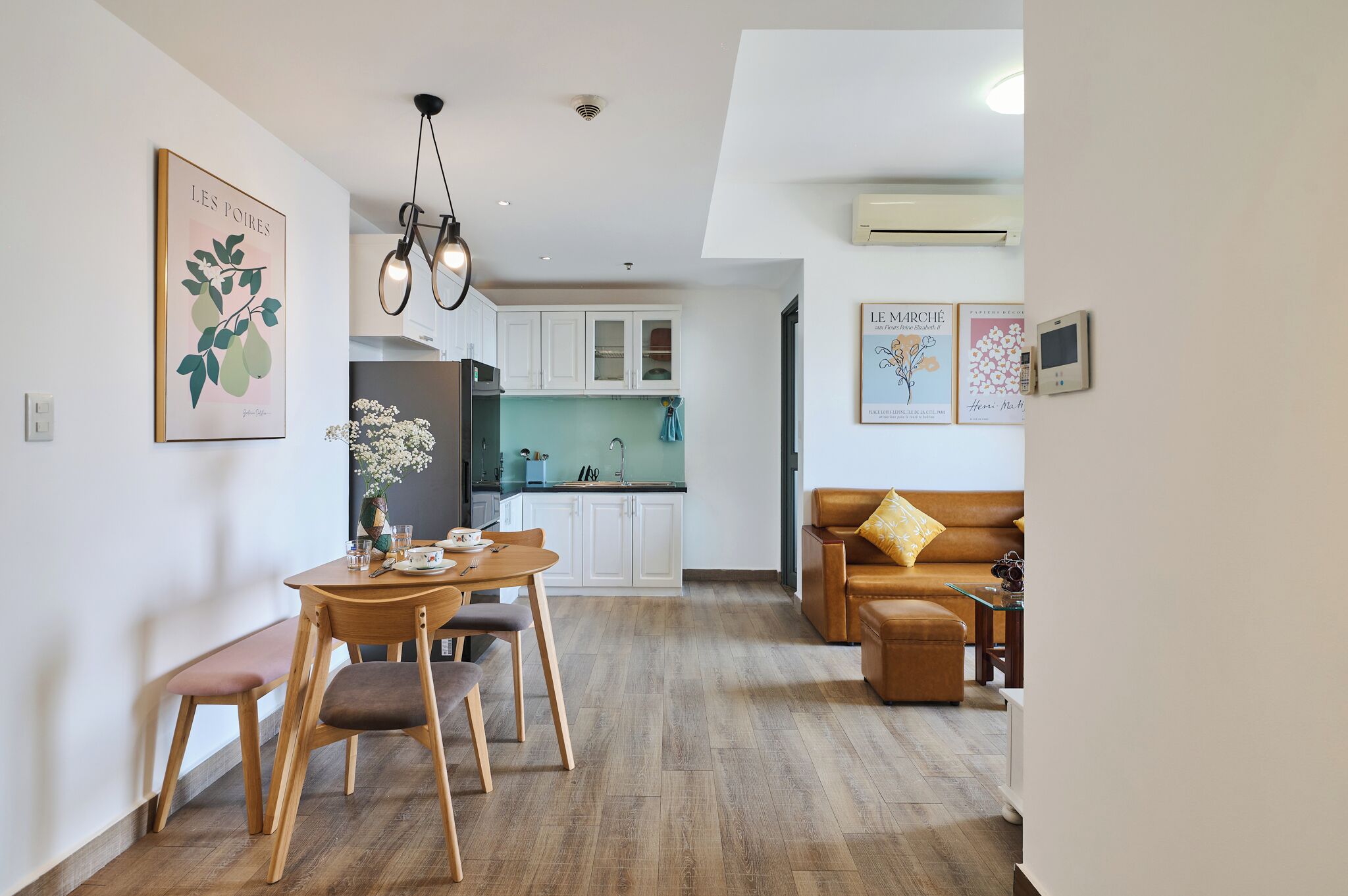A modern living room with a dining area, a kitchen in the background, and a brown leather sofa.