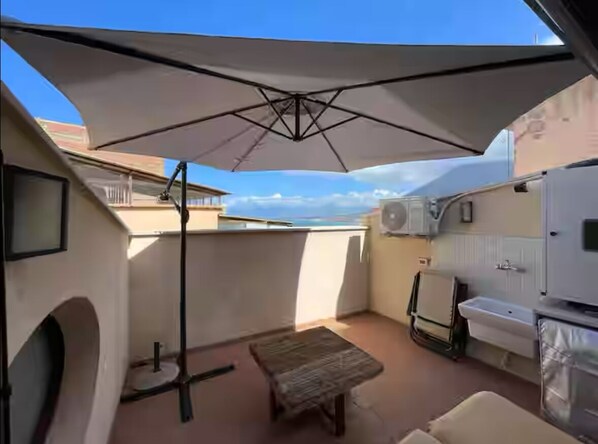 A compact balcony with a white umbrella, a small table, and a sink.
