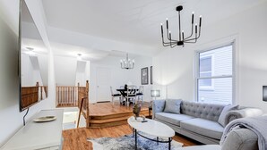 A spacious living room with a grey sofa, a coffee table, and a dining area with a white table and chairs. - Charming 2-bedroom, 1 bath apartment in historic Cabbagetown (Toronto)