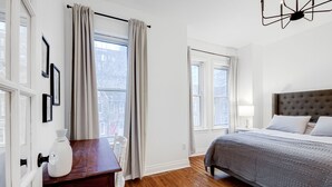 A bedroom with a large bed, a wooden dresser, a white vase, and a window with curtains. - Charming 2-bedroom, 1 bath apartment in historic Cabbagetown (Toronto)