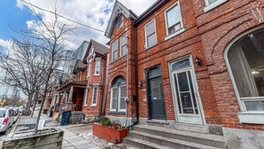 A row of red brick townhouses with large windows and a front porch. - Charming 2-bedroom, 1 bath apartment in historic Cabbagetown (Toronto)