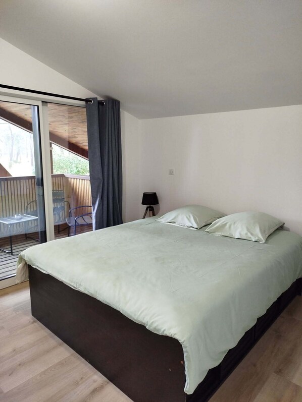 Une chambre avec un grand lit, une petite table de chevet, une lampe et une vue sur une terrasse extérieure.