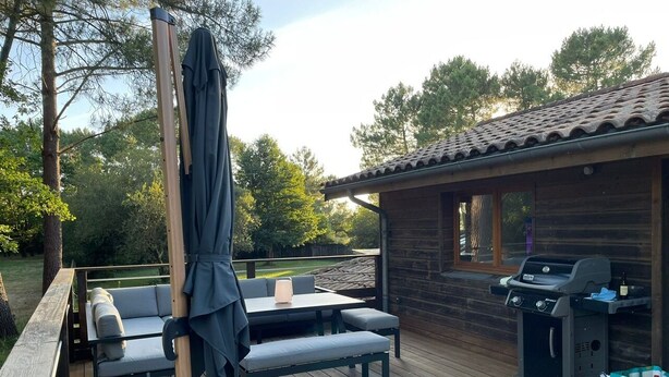 Eine Terrasse im Freien mit Holztisch und -bänken, einem Grill und einem überdachten Sitzbereich.