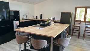 Eine moderne Küche mit einer zentralen Kochinsel, Barhocker, einem Kühlschrank und einem Fenster, das natürliches Licht hereinlässt.