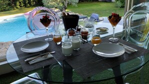 A dining table set for two with a glass top, surrounded by chairs, near a pool. - Crémieu, calm and relaxation, 2 steps from the center. (Crémieu)