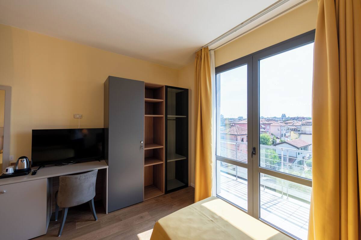 Una habitación de hotel moderna con escritorio, televisión y un amplio ventanal con cortinas.