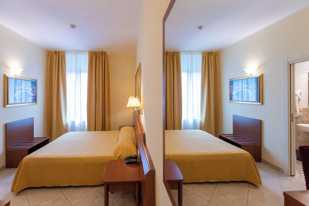 Una habitación de hotel con dos camas, una mesita de noche, una lámpara y un espejo.