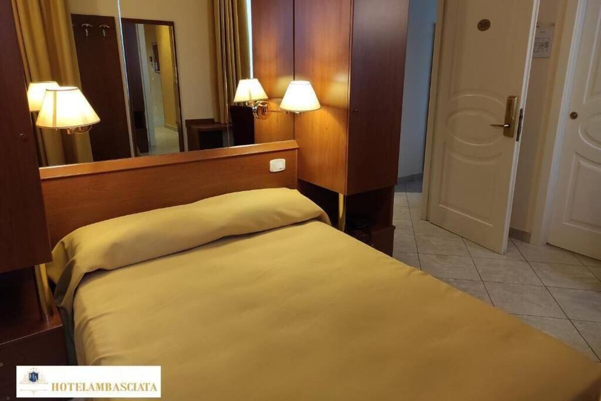 Una habitación de hotel con una cama, dos lámparas de noche, un espejo y una puerta.