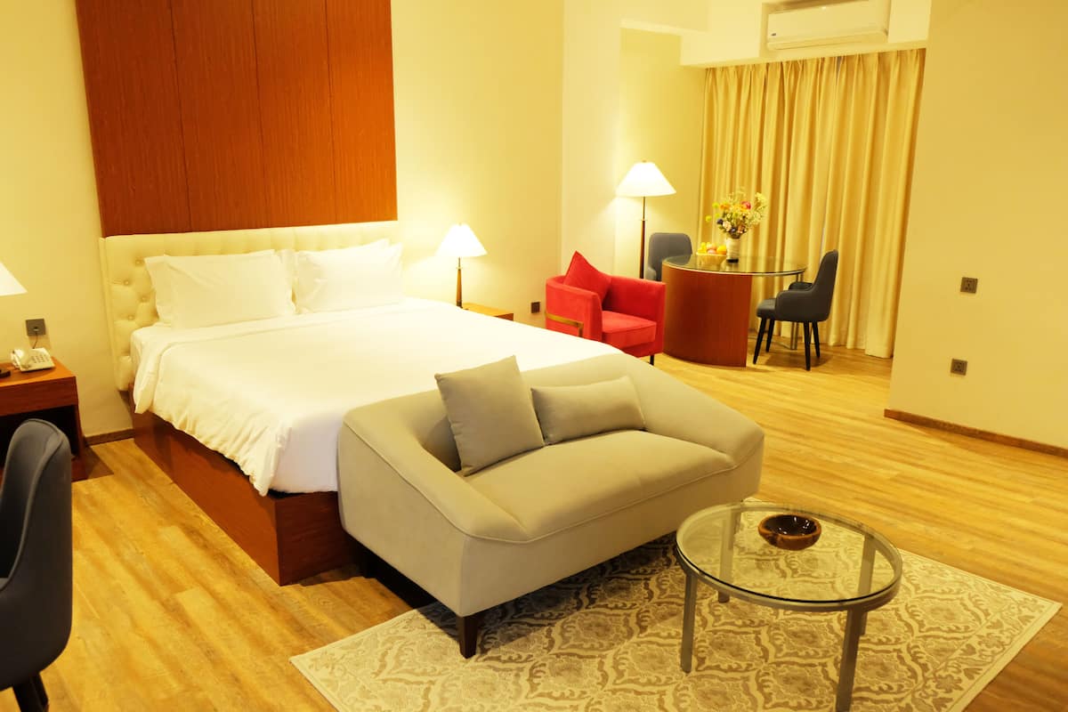Une chambre d’hôtel comprenant un lit, un canapé, une table basse en verre, un bureau avec une lampe et une chaise.