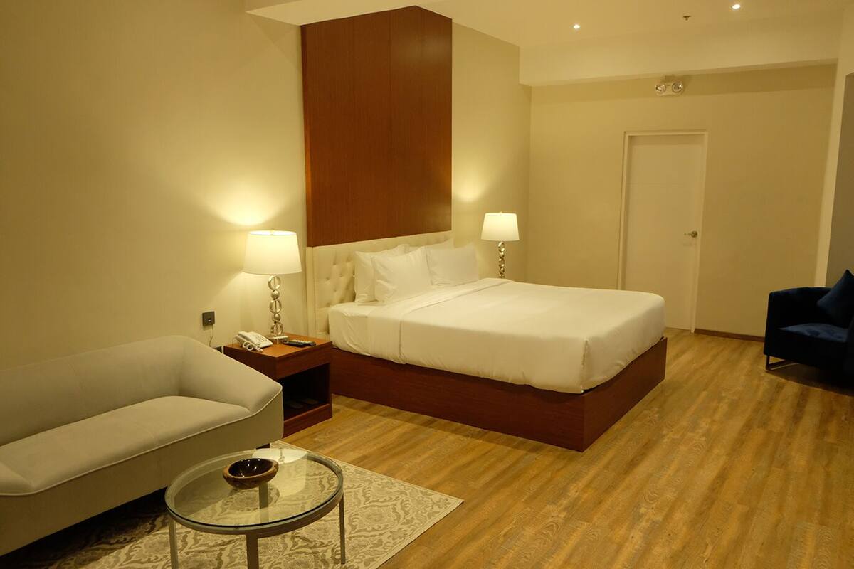 Une chambre d’hôtel avec un lit, une table de chevet, une lampe, un canapé, une table basse et une porte.