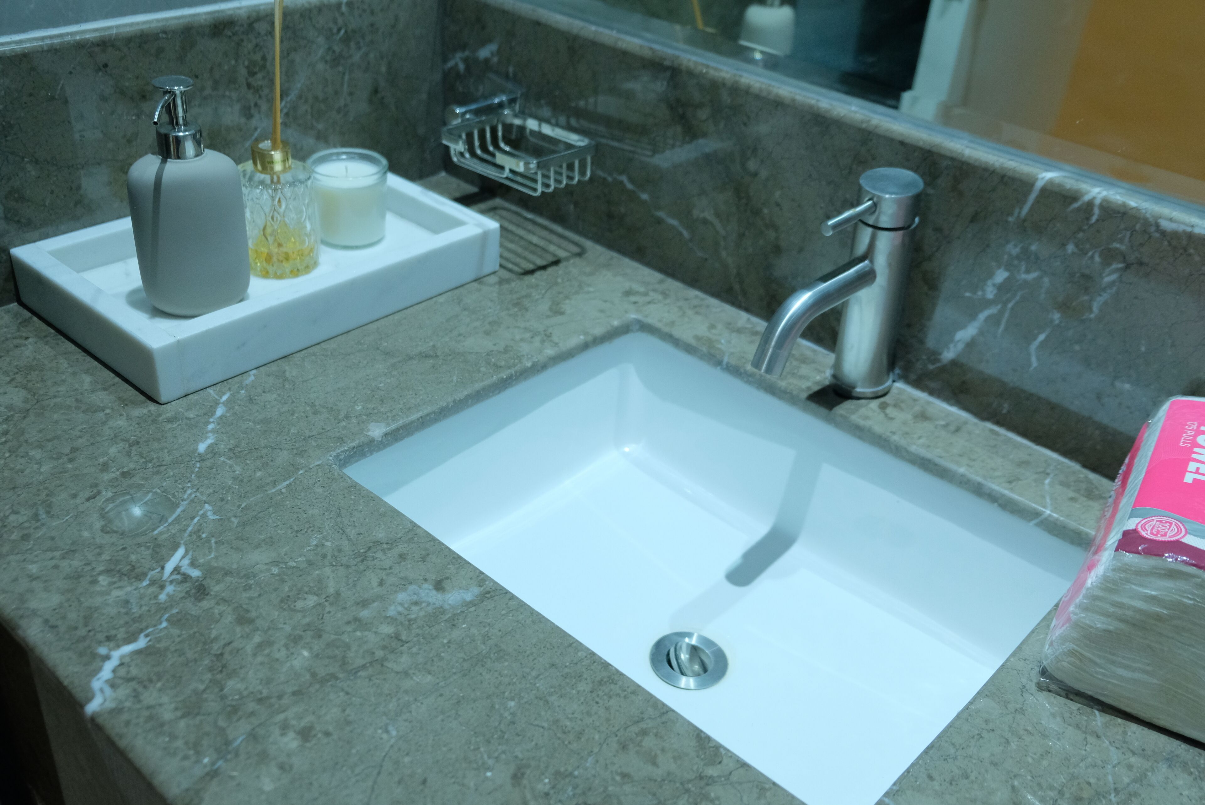 Ein Badezimmer mit einem weißen Waschbecken, einem Spiegel und einer Seifenspender auf einer Marmorplatte.