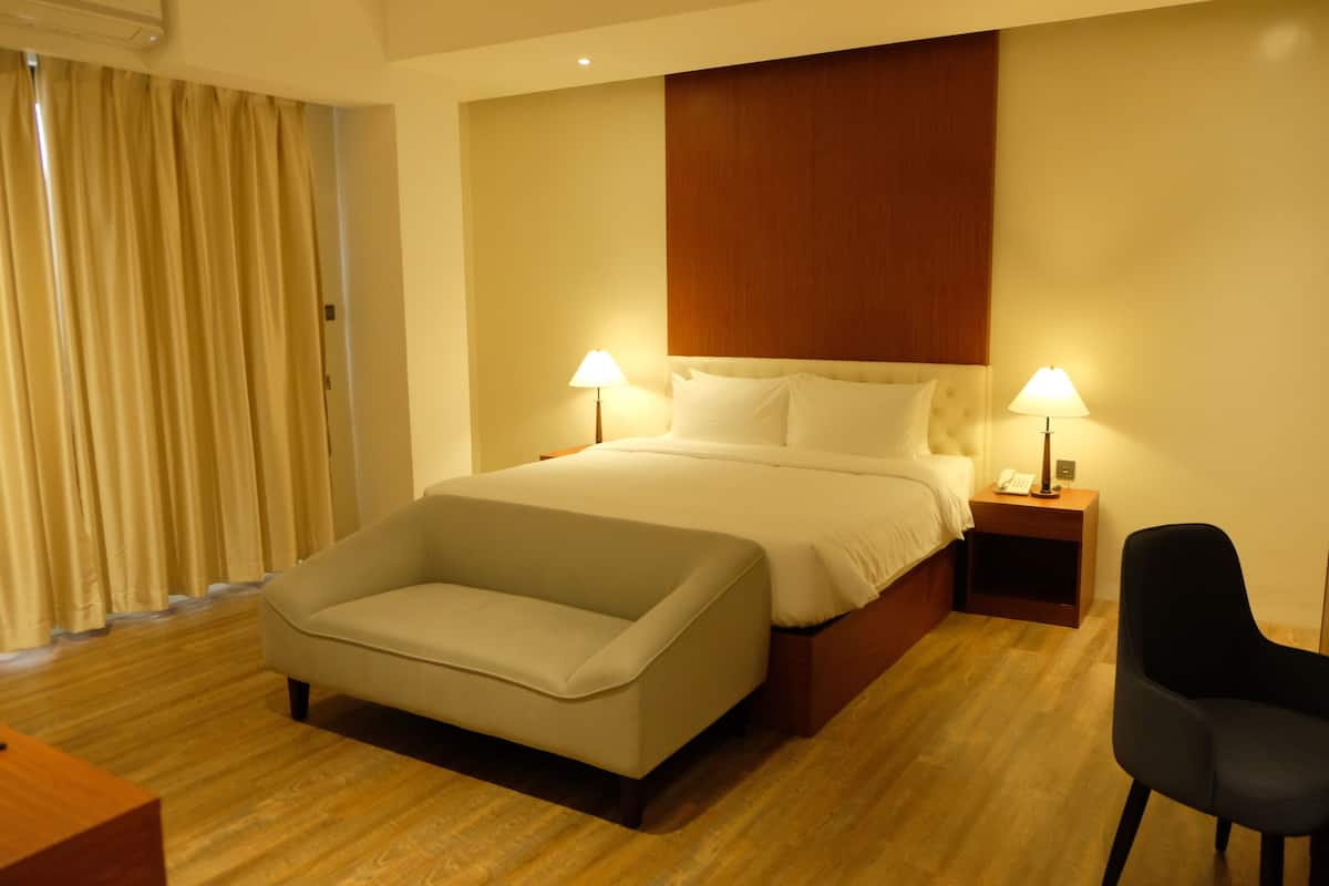 Une chambre d’hôtel avec un lit, deux lampes de chevet, un canapé, un fauteuil et un plancher en bois.
