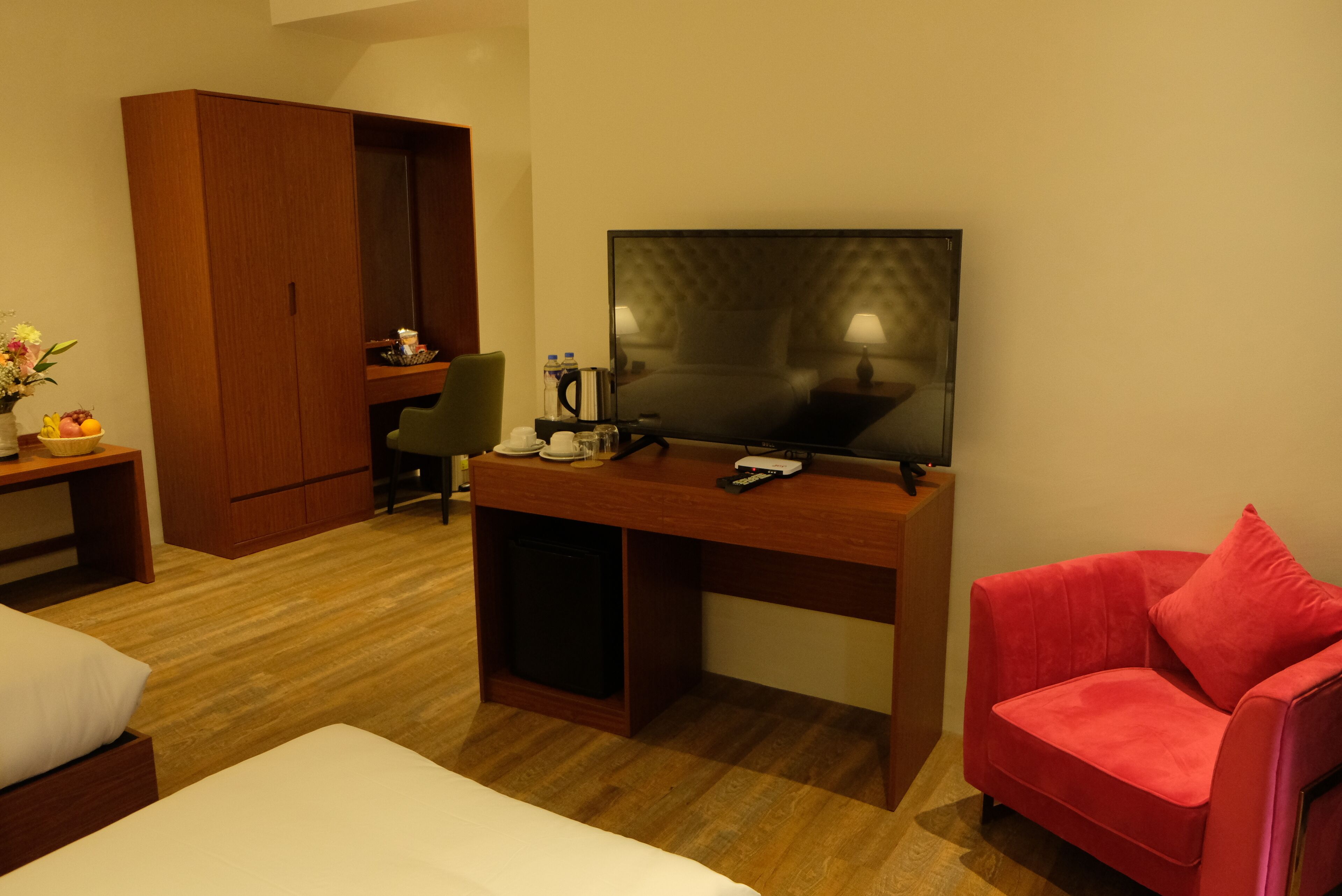 A hotel room with a bed, a desk with a television, a red chair, and a wardrobe.