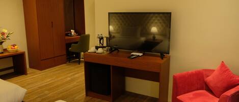 A hotel room with a bed, a desk with a television, a red chair, and a wardrobe.
