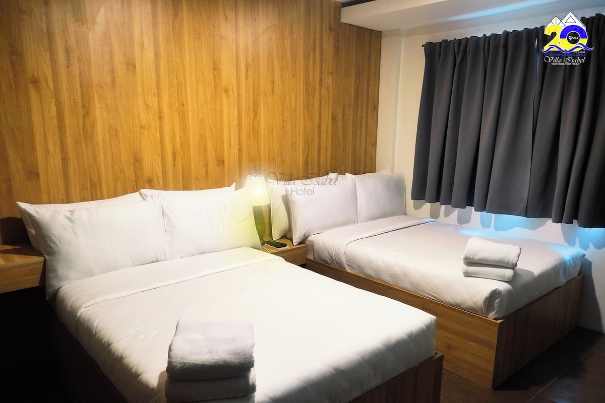 Une chambre d’hôtel avec deux lits, des lambris en bois aux murs, une table de chevet avec une lampe et une fenêtre avec des rideaux foncés.