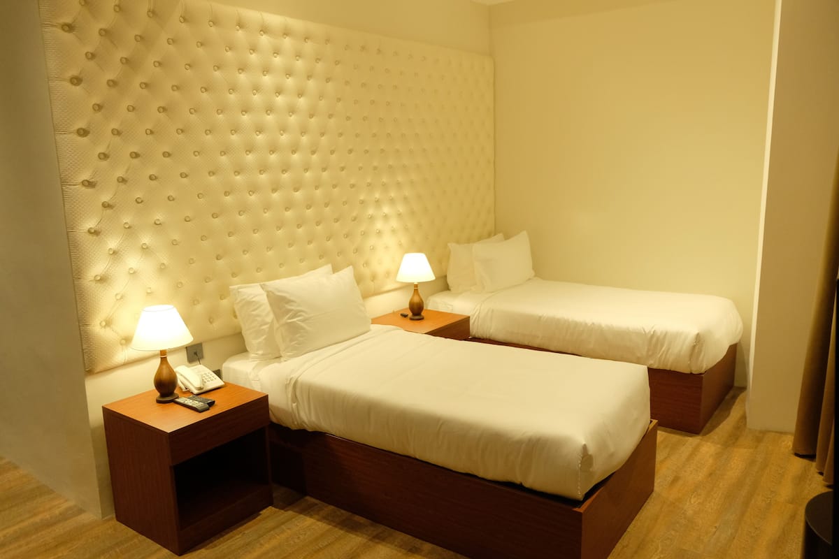 Une chambre d’hôtel avec deux lits simples, une tête de lit capitonnée, des lampes de chevet et un plancher en bois.