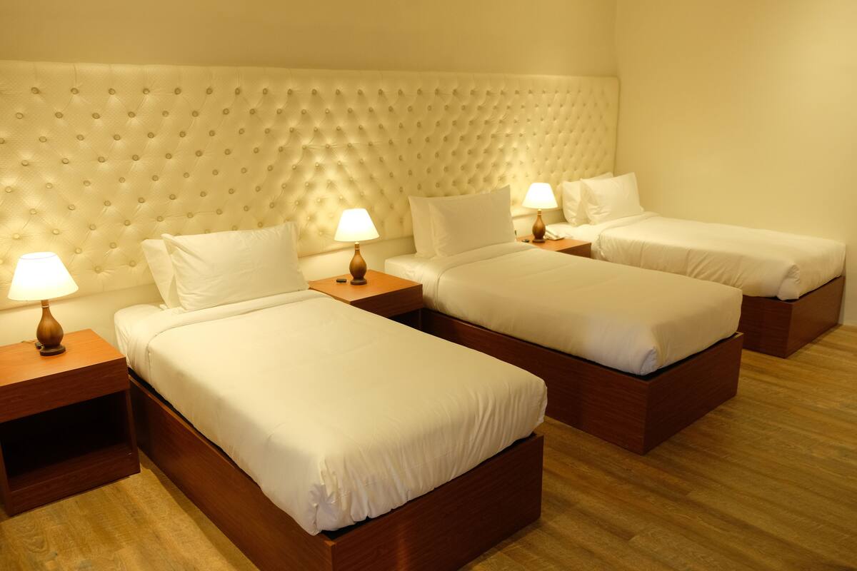 Une chambre d’hôtel avec une tête de lit capitonnée, deux lits avec du linge de lit blanc, des tables de chevet en bois et des lampes de chevet.