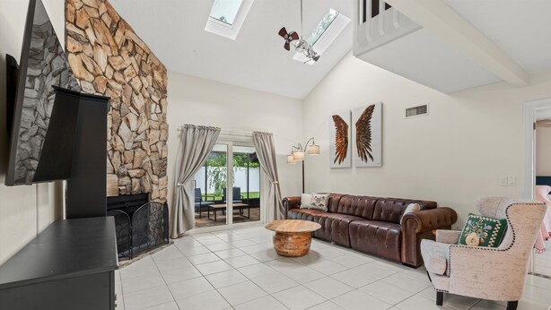 A spacious living room with a stone wall, a leather sofa, a coffee table, and a television. -  Saltwater Pool I Firepits I Large Fenced Backyard I 4 Miles to Beach (Jacksonville)