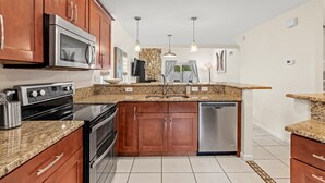 A kitchen with wooden cabinets, granite countertops, stainless steel appliances, and pendant lighting. -  Saltwater Pool I Firepits I Large Fenced Backyard I 4 Miles to Beach (Jacksonville)