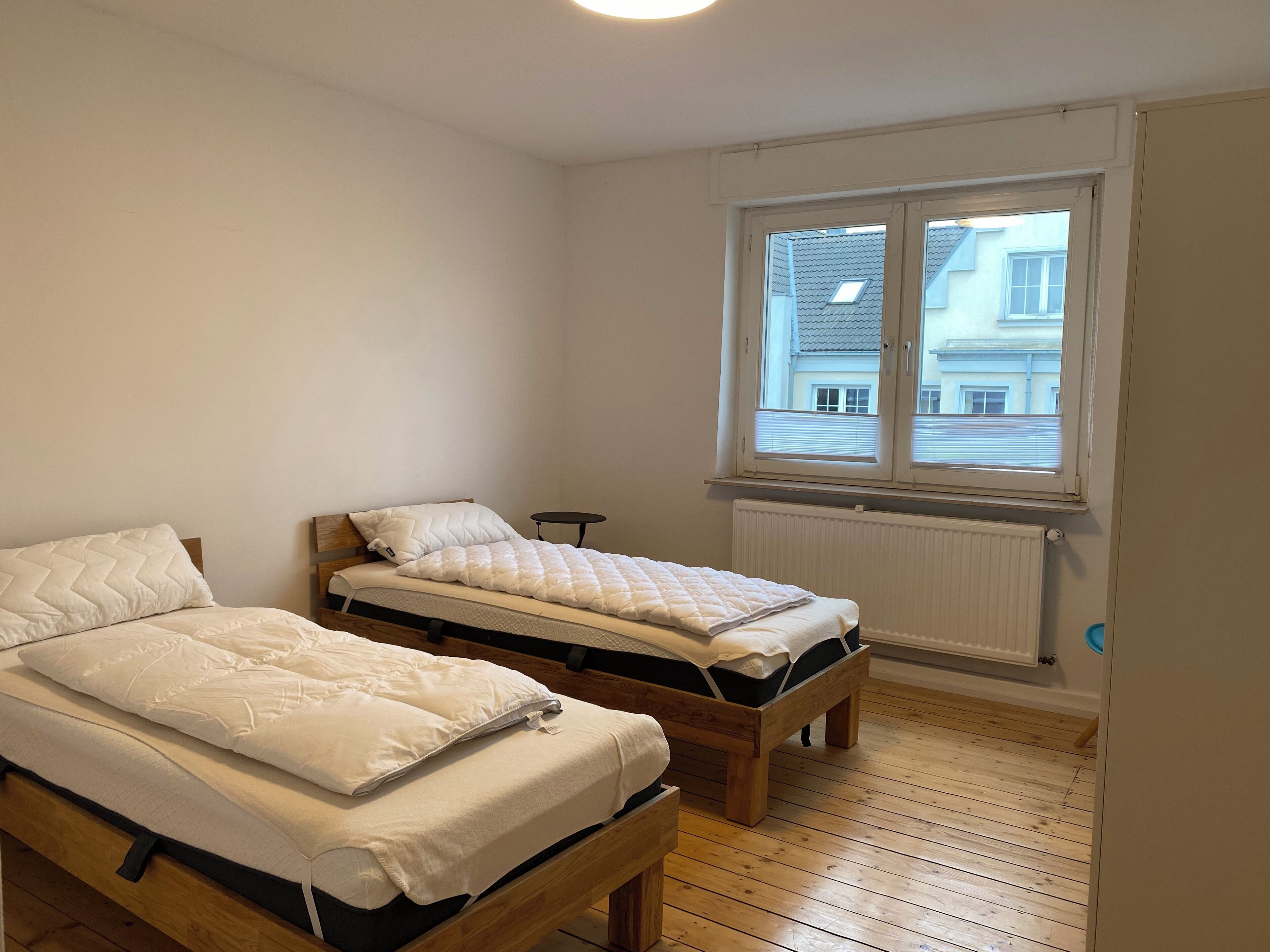 Ett rum med två sängar i trä, ett litet runt bord och ett fönster med persienner.