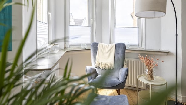 A room with a grey armchair, a floor lamp, and a table with a vase of dried flowers. - Gemütliches wohnen in idealer Lage, nahe Dortmund! (Holzwickede)