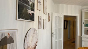 A room with a wooden floor, white walls, and a door leading to another room. There are several framed pictures on the wall. - Gemütliches wohnen in idealer Lage, nahe Dortmund! (Holzwickede)
