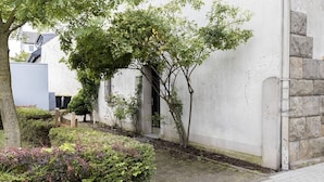 A courtyard with a tree, a small garden area, and a building with a stone wall. - Gemütliches wohnen in idealer Lage, nahe Dortmund! (Holzwickede)