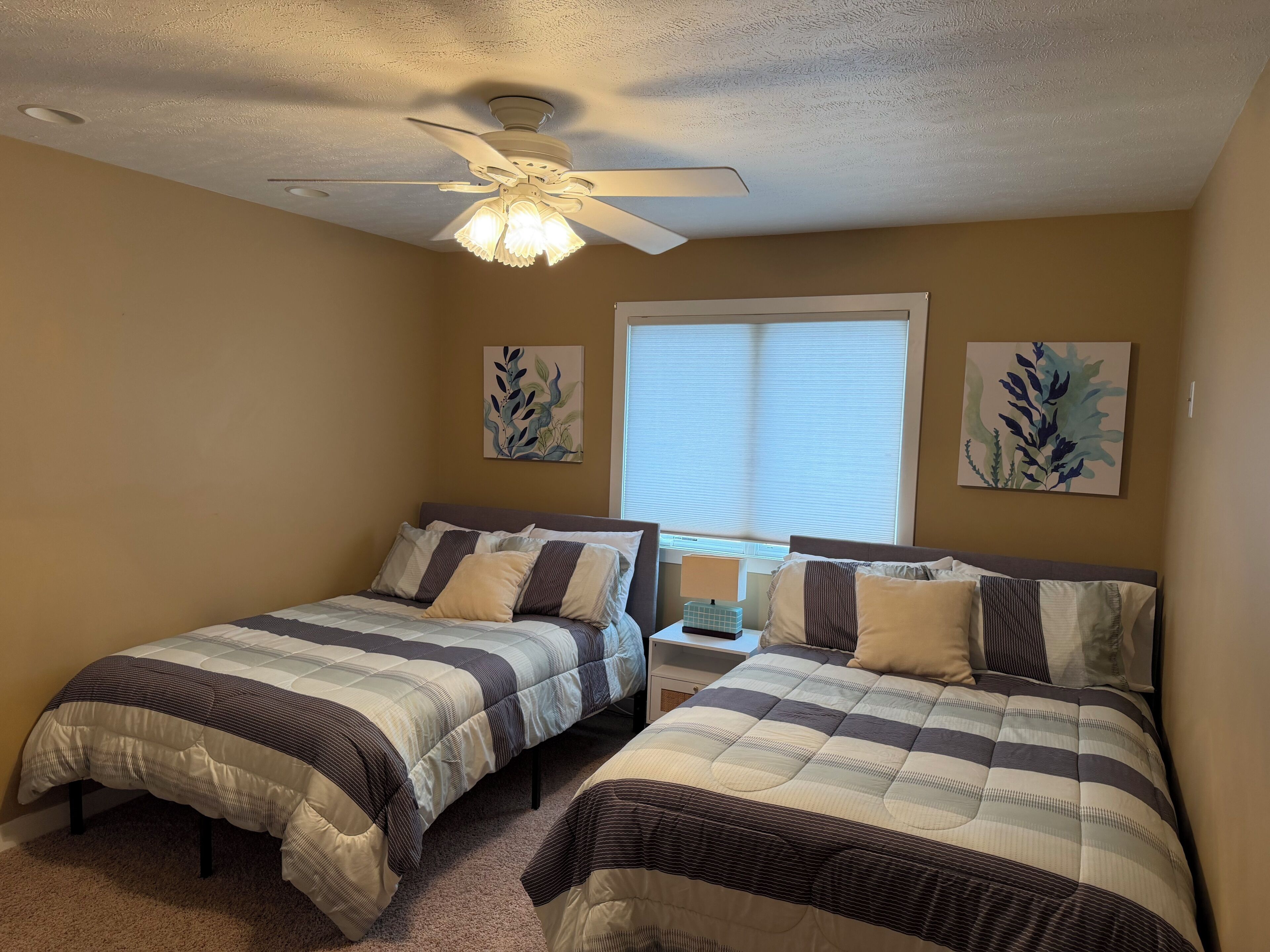 A bedroom with two beds, a ceiling fan, and artwork on the walls.