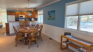 A dining area with a round table and chairs, a kitchen in the background, and a window with blinds. - Stunning Lake Views with Balcony - with lake access (Allegan)