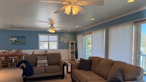 A living room with two sofas, a ceiling fan, and a dining area with a table and chairs. - Stunning Lake Views with Balcony - with lake access (Allegan)