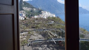 Une vue à travers une fenêtre sur une ville côtière, avec ses bâtiments, une montagne et la mer.
