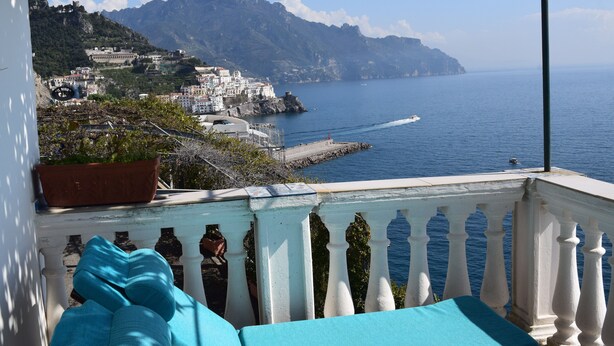 Un balcon donnant sur une ville côtière, une plante en pot et une balustrade blanche.