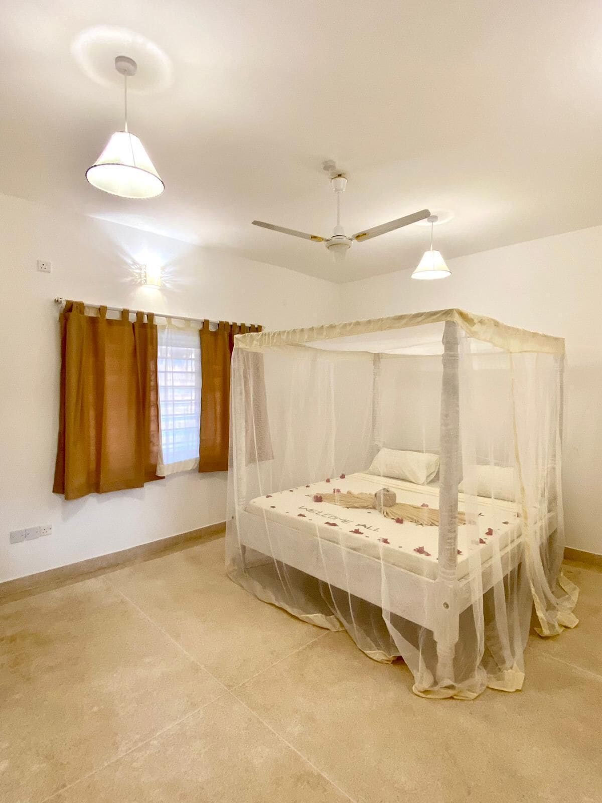 A bedroom with a four-poster bed, a ceiling fan, and a window with curtains.