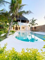 A modern resort with a pool, palm trees, and a thatched-roof structure.